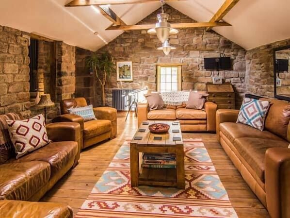A cozy living room with stone walls, leather sofas, and a wooden coffee table. - The Malthouse (Matlock)