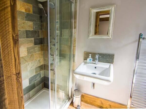 A bathroom with a glass shower enclosure, a white sink, and a mirror on the wall. - The Malthouse (Matlock)
