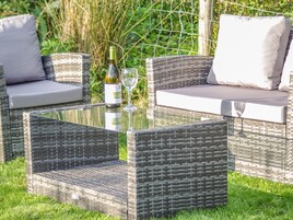 A wicker outdoor seating area with cushions and a glass table, set on a grassy lawn.