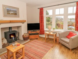 A cozy living room with a fireplace, a television, a comfortable sofa, and a view of the outdoors through large windows.