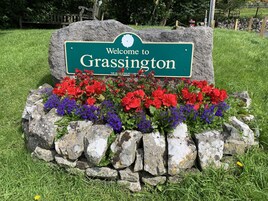 A welcome sign to Grassington with a stone border and colorful flowers.