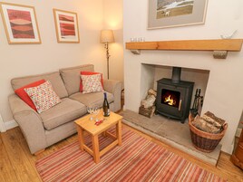 A cozy living room with a sofa, a small table with glasses and a bottle, a fireplace, and framed pictures on the wall.