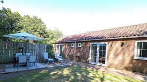 A backyard with a patio, a wooden fence, and a brick house with a tiled roof. - Mill Lodge, Brisley Accessible Norfolk Cottage Sleeping 6, Dog-friendly (Dereham)