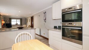 Une cuisine moderne avec des meubles blancs, un four encastré et un coin repas doté d’une table en bois.