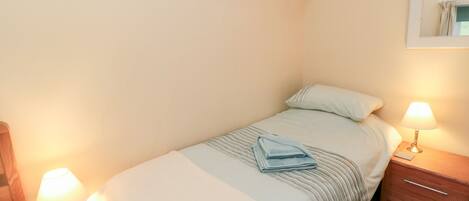 A single bed with a white and light blue bedspread, two bedside lamps, a wooden nightstand, and two framed pictures on the wall.
