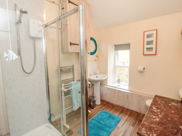 A bathroom with a glass shower enclosure, a sink, a toilet, and a blue rug on the floor. - Ghyll Cottage (Pickering)