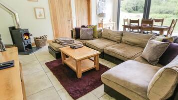 Un salon chaleureux avec un canapé, une table basse en bois et une cheminée. Il y a deux portes et une fenêtre donnant sur un paysage verdoyant.