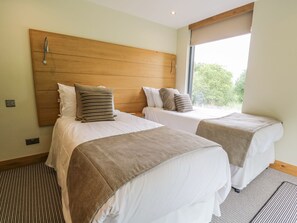 A hotel room with two beds, wooden headboards, and a large window providing a view of greenery outside. - Neddy Cut (Ulverston)
