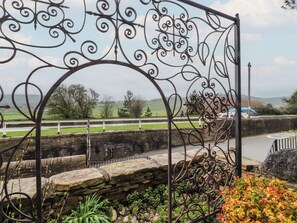 A metal gate with intricate designs, a stone wall, and a view of a road with a vehicle.