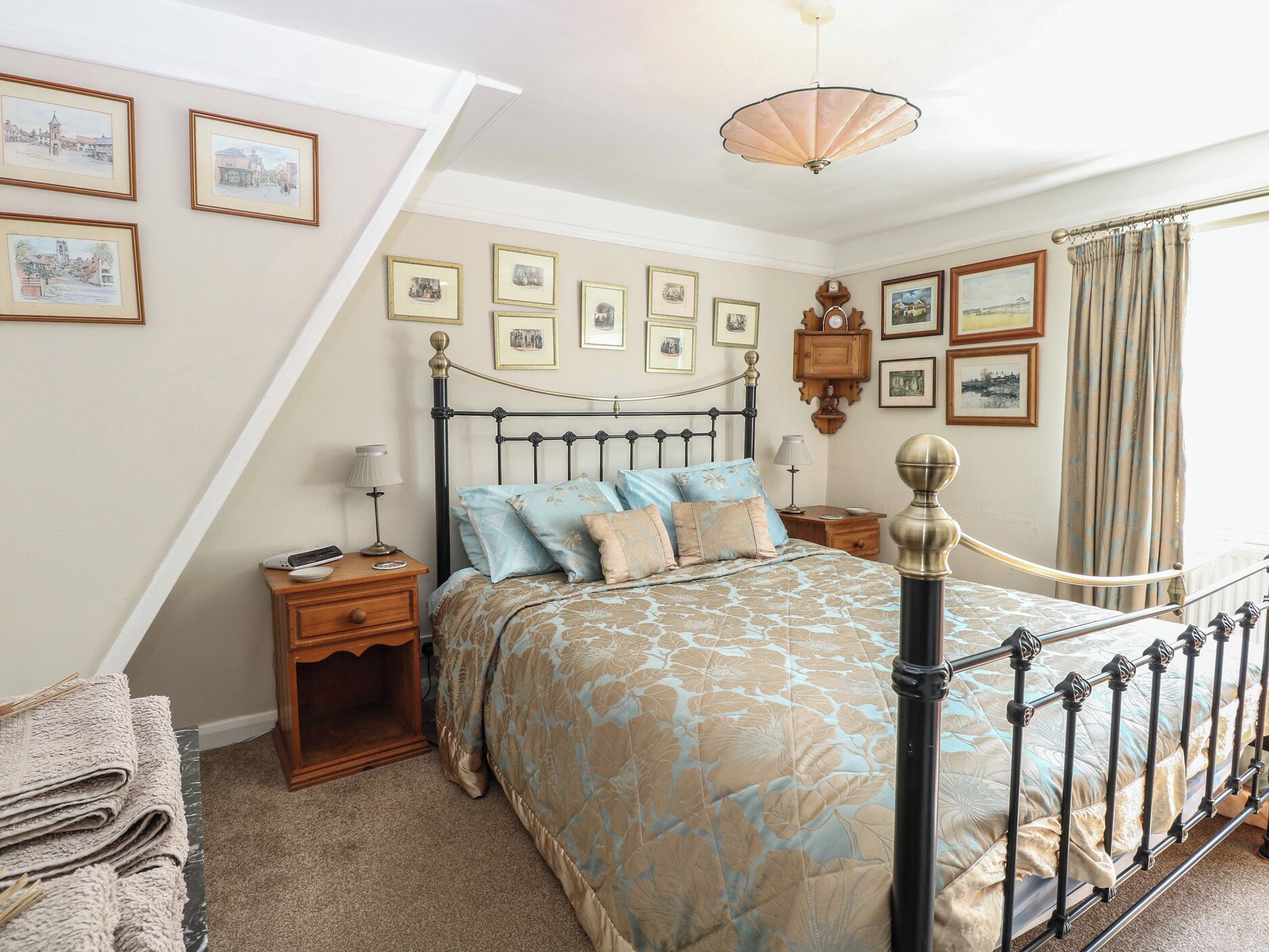 A bedroom with a bed, bedside tables, lamps, a wooden cabinet, and framed pictures on the walls.