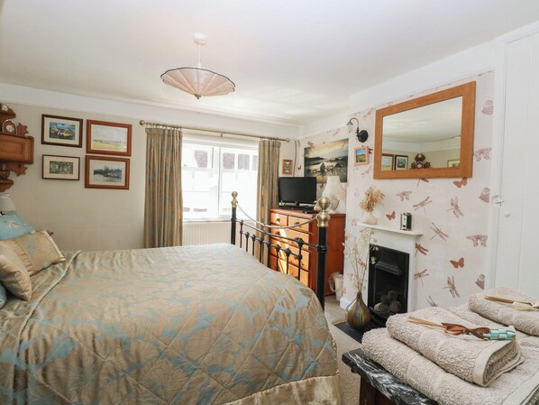 A bedroom with a bed, dresser, television, fireplace, and a mirror. - Peggotty's (Saxmundham)
