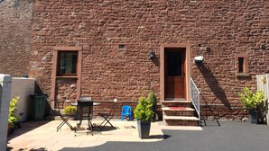 A stone building with a wooden door and windows, a small outdoor seating area with a table and chairs, and a potted plant. - The Old Bothy (Wigton)