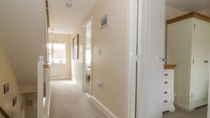 A hallway with carpeted floors, white walls, and a white door leading to a room with a wooden cabinet.
