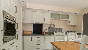 A modern kitchen with white cabinetry, a built-in oven, and a dining area with a wooden table and chairs.