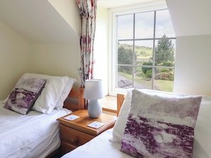 Une chambre avec deux lits, une table de chevet, une lampe et une fenêtre donnant sur un paysage verdoyant.