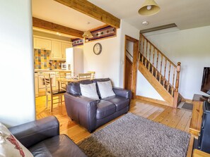 A living room with a dark leather sofa, a wooden staircase, and a kitchen in the background.