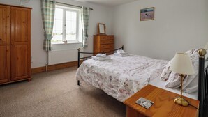 Une chambre à coucher comprenant un lit, une commode, un radiateur, une fenêtre avec des rideaux, un tableau accroché au mur et une table de chevet avec une lampe.
