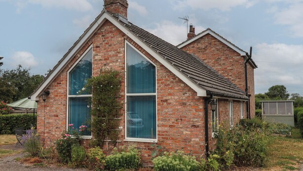 Une maison à deux étages, construite en briques, avec un toit à pignon, de grandes fenêtres et une cheminée.