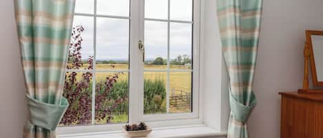 A window with a view of a rural landscape, curtains, a radiator, and a wooden cabinet.