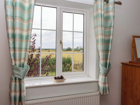 Una ventana con vista a un paisaje rural, cortinas, un radiador y un armario de madera.