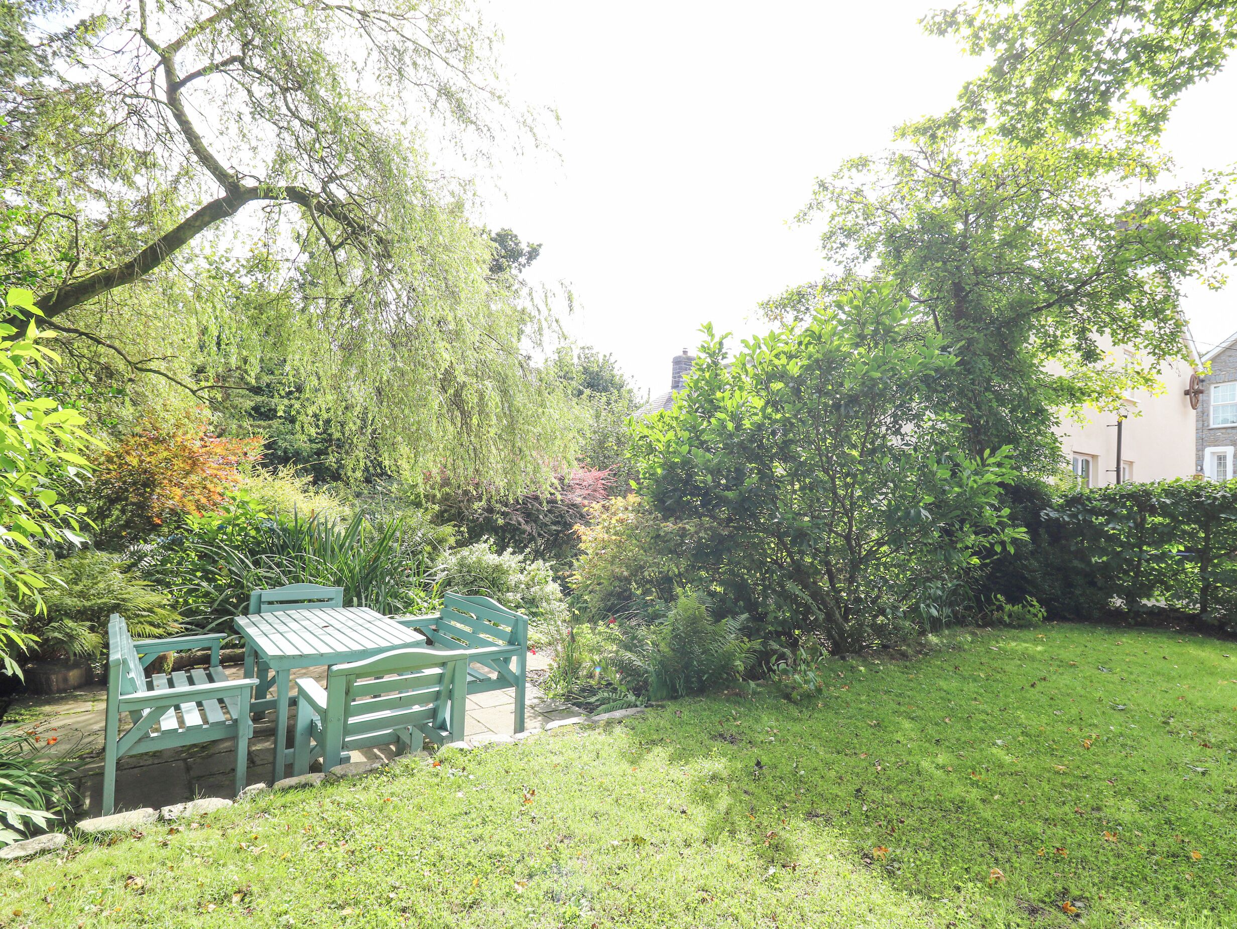 A garden with a wooden bench and table, surrounded by various plants and trees.