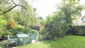 A garden with a wooden bench and table, surrounded by various plants and trees.