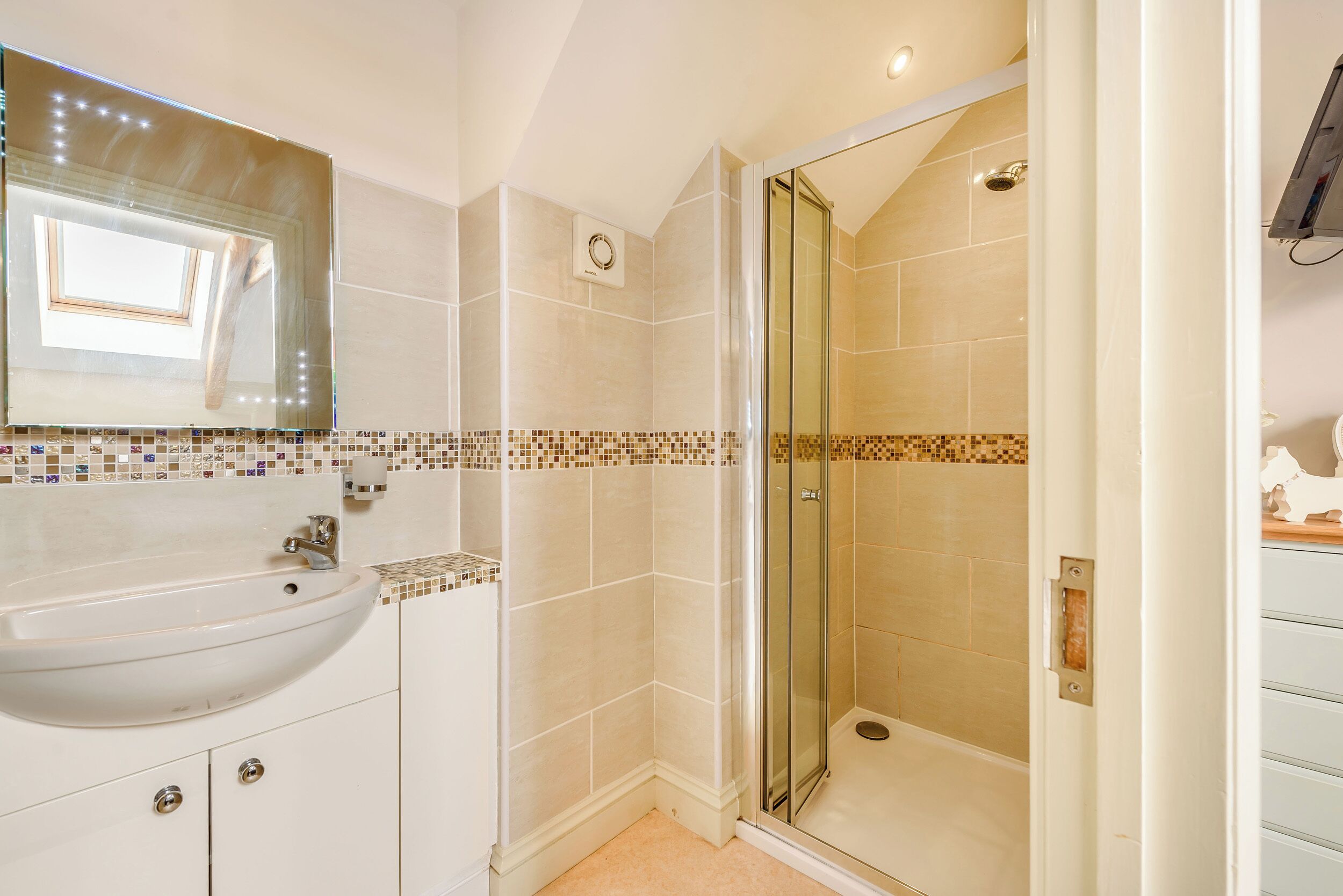 A bathroom with a glass-enclosed shower, a sink with a mirror above it, and tiled walls.