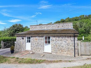 A stone cottage with two doors, a small porch, and a wooden fence.