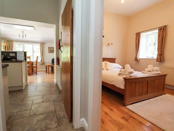A hotel room with a wooden bed, a bedside table, a window with curtains, and a view of the outdoors. - The Lambing Shed (Rhyl)