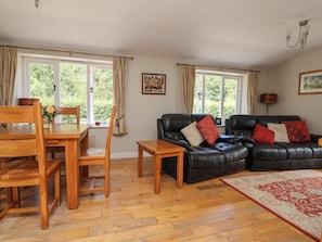 A living room with a wooden dining table, two black leather sofas, and a red patterned rug. - The Lambing Shed (Rhyl)
