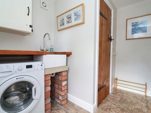A laundry area with a washing machine, a sink, and a wooden door. - The Lambing Shed (Rhyl)