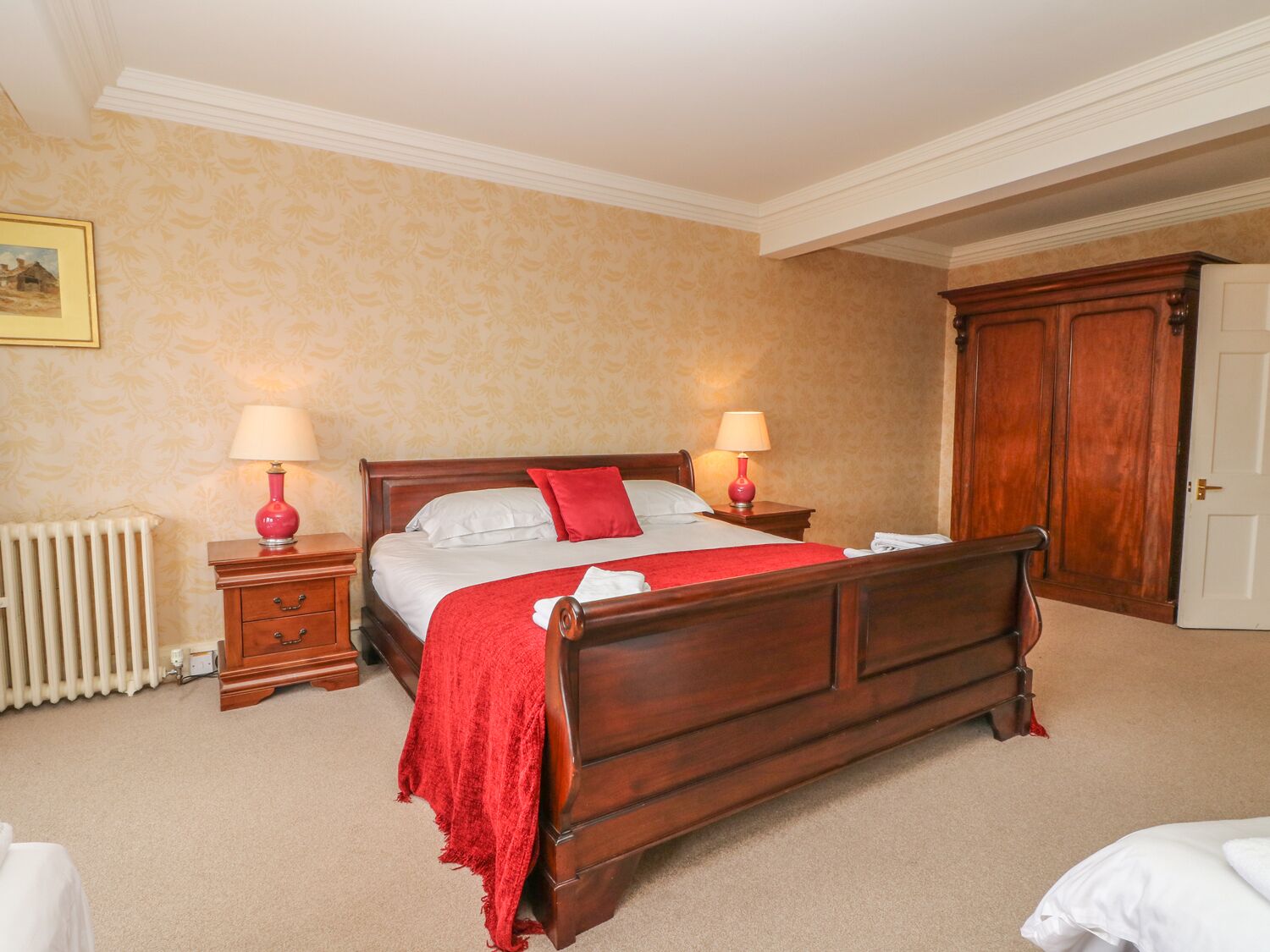 Een keurig opgemaakt slaapkamer met een houten bed, twee nachtkastjes met lampen, een radiator en een kledingkast.