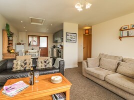 A cozy living room with a leather sofa, a beige sofa, and a wooden coffee table with newspapers and a bottle.