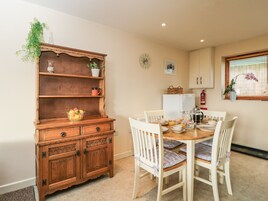 A dining area with a wooden cabinet, a table set with chairs, a clock, and a window with blinds.