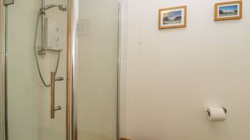 A bathroom with a glass shower enclosure, a wooden bench, and two framed pictures on the wall.