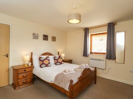 A bedroom with a wooden bed, bedside tables, a nightstand, a window with curtains, and a wall-mounted heater.