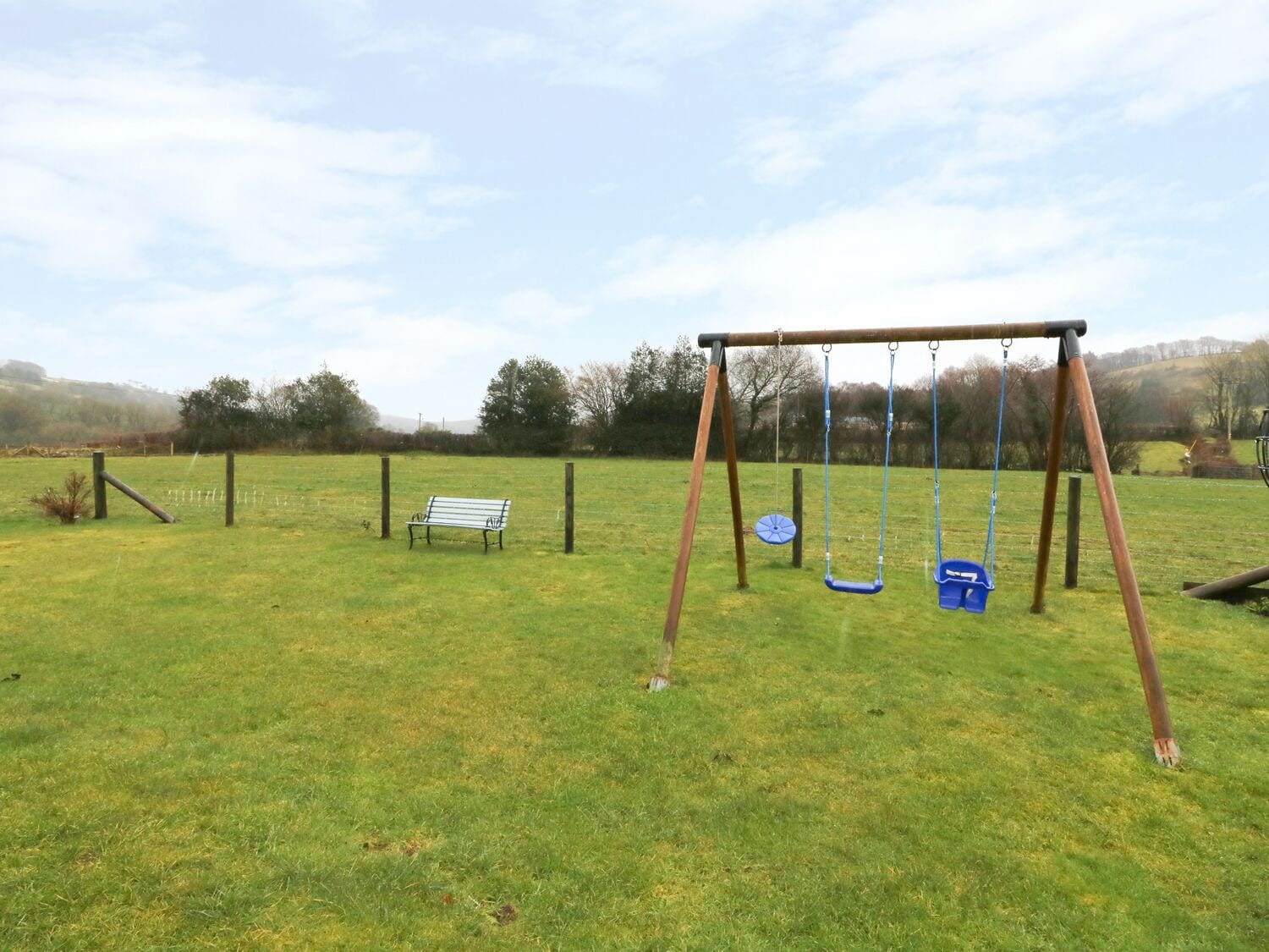 A grassy field with a swing set and a bench.
