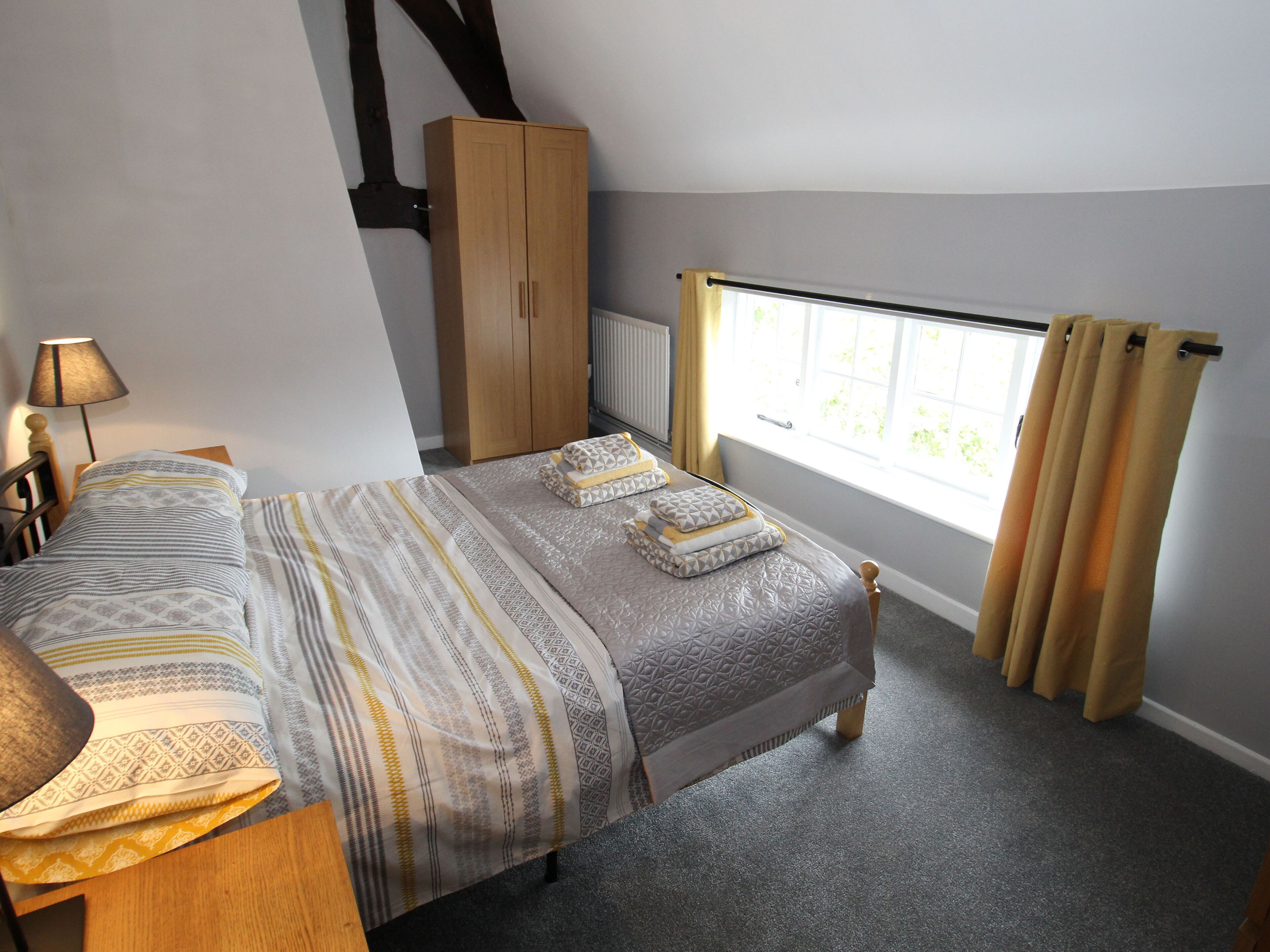 A bedroom with a bed, a wardrobe, a window with curtains, and a lamp.