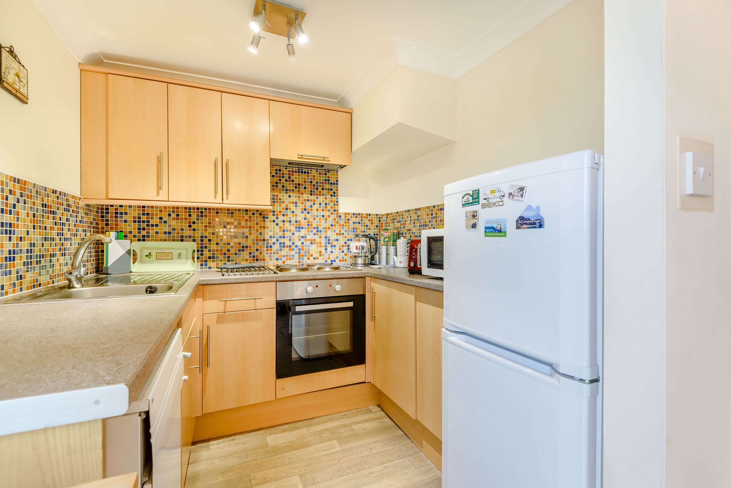 Una cocina compacta con armarios de madera, horno empotrado, refrigerador y salpicadero de azulejos.