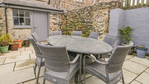 Un bâtiment en pierre avec une table ronde et des chaises en osier dans une cour.