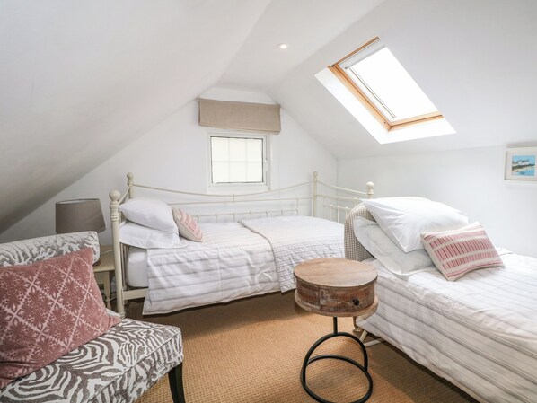 A bedroom with a sloped ceiling, a skylight, a bed with a headboard, a bedside table, and a patterned chair. - Woodend Annexe (Arundel)