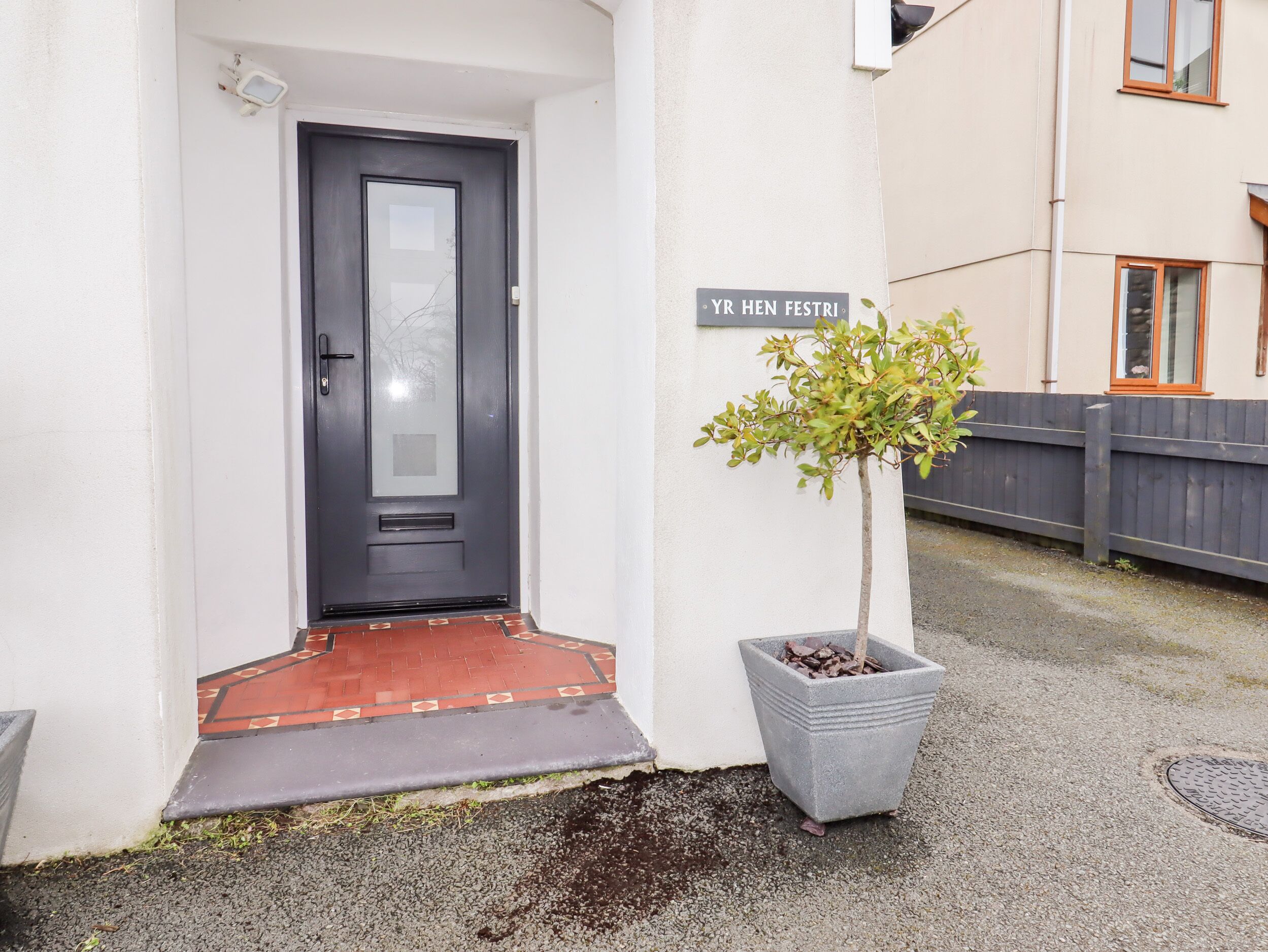 Une porte sombre, avec un petit seuil, un pot de fleurs placé à côté de la porte et une enseigne au-dessus.