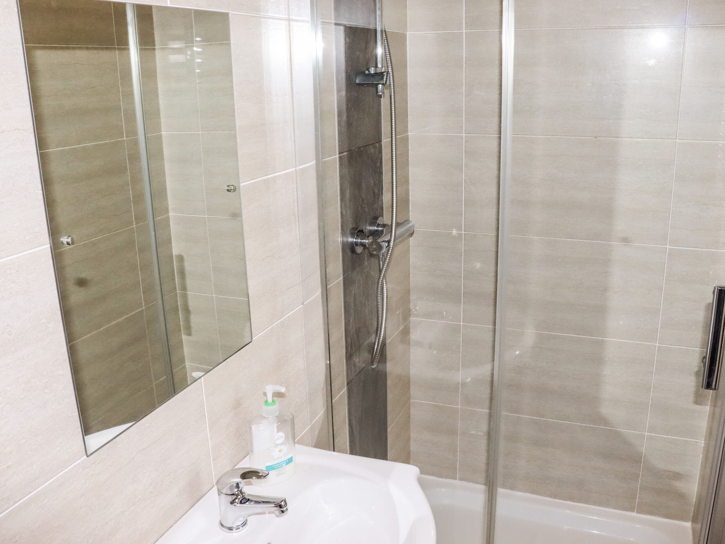 Un baño con cabina de ducha de vidrio, un lavabo blanco y un espejo.