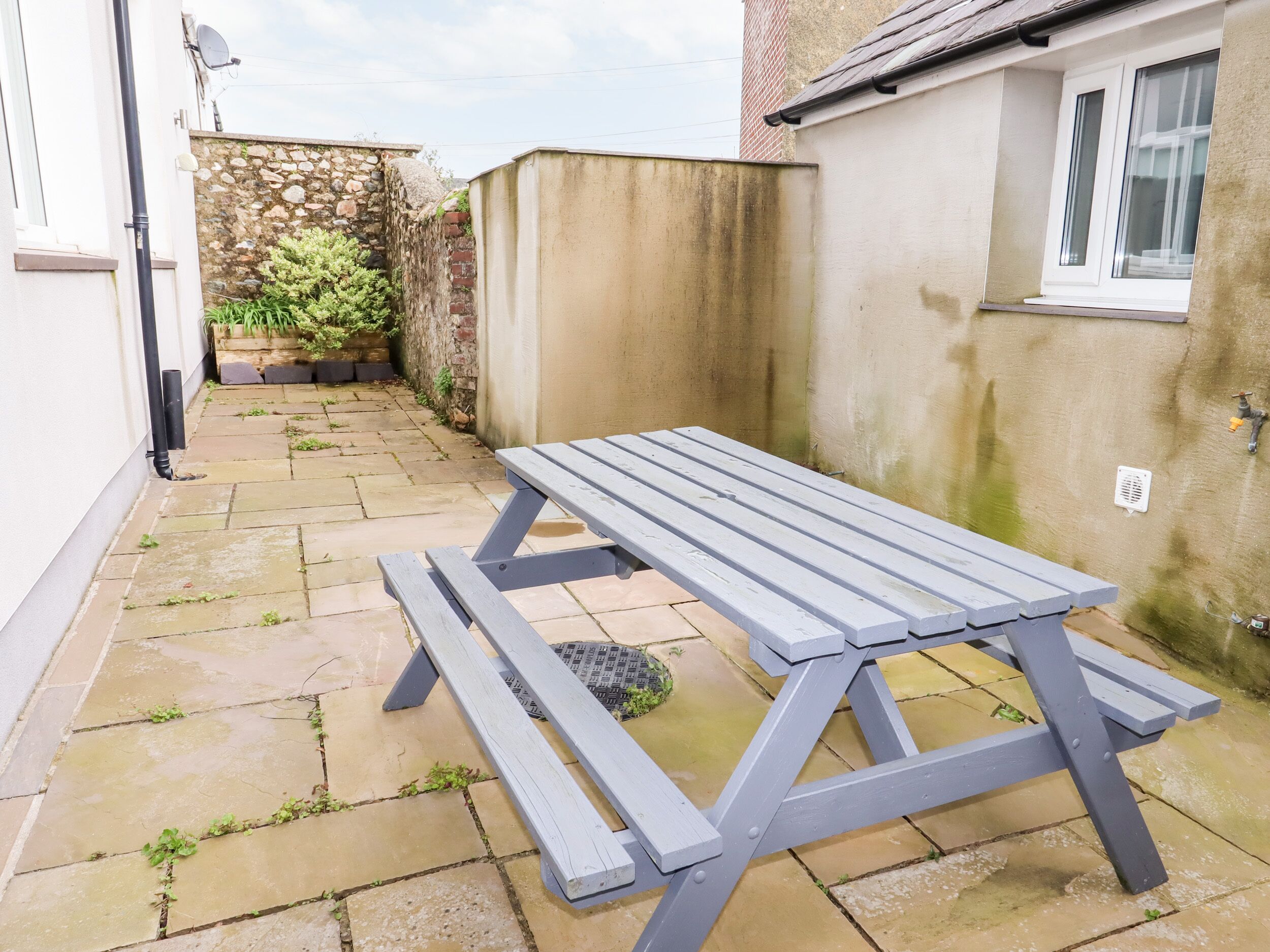 Eine Terrasse mit einem Holztisch und Bänken, einer Steinmauer und einem kleinen Garten.