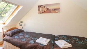 A bedroom with a single bed, a bedside table, a lamp, and a painting of a coastal scene. - Garth Morthin The Stables (Porthmadog)