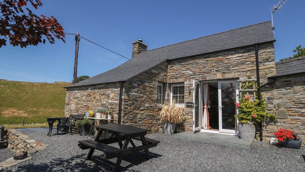 A stone building with a gravel patio, a picnic table, and potted plants. - Garth Morthin The Stables (Porthmadog)