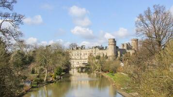 A historic castle with a moat, surrounded by trees and a river.
