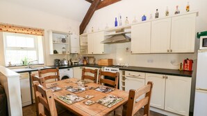 Een keuken met houten stoelen, een eettafel, witte kasten, een fornuis en diverse keukenapparaten.