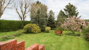 A well-maintained garden with a variety of trees and shrubs, a wooden bench, and a brick wall. - The Old Grocery (Chesterfield)