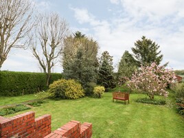 A well-maintained garden with a variety of trees and shrubs, a wooden bench, and a brick wall.